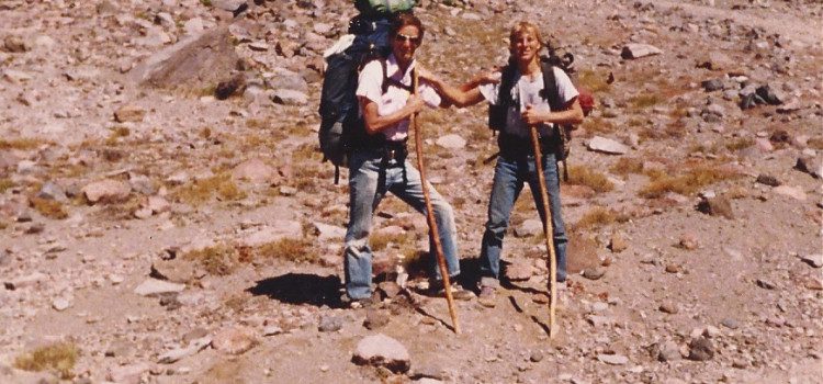 Two men standing on a rocky hillside with backpacks.